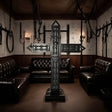 Luxury padded black BDSM cross displayed in a premium dungeon lounge with dark leather seating, wall-mounted restraints, and moody ambient lighting. High-end freestanding St. Andrew’s cross for luxury BDSM room design and professional dungeon setups.