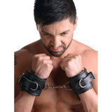 Padded leather wrist restraints worn on a model's wrists - BDSM Authority